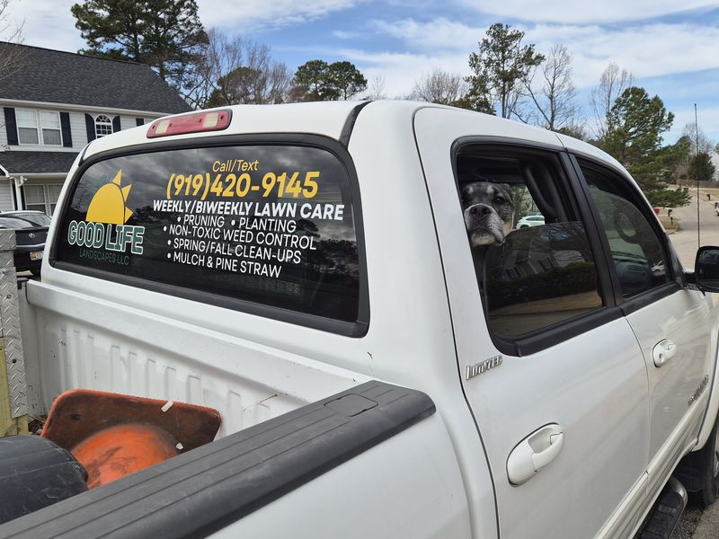 The white Good Life Landscapes truck with the phone number on the back window